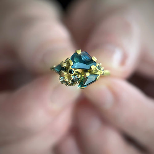 Tidepool ring with sapphire gemstones held between fingers against a blurred background